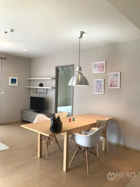 Condominium for rent or sale in Watthana, Bangkok - Bright dining area with wooden table, white chairs and a pendant light next to the TV corner.