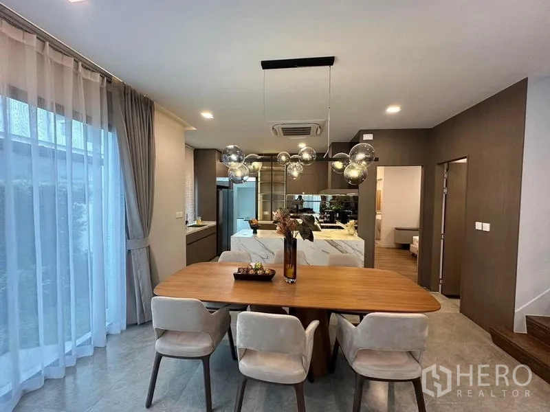 Detached House for rent in Samut Prakan - Dining area beside modern kitchen with marble island and cabinetry.