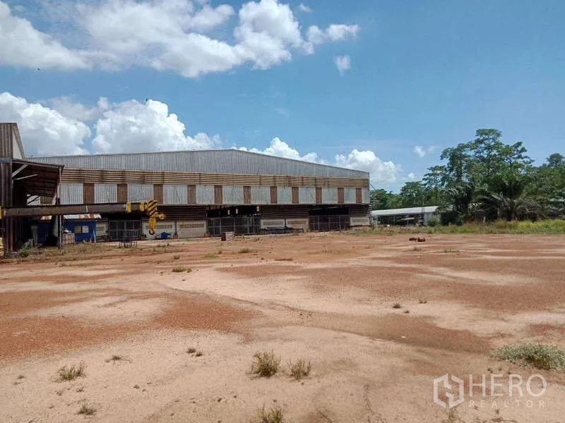 Factory for sale in Chachoengsao - Warehouse exterior beside an open soil yard with surrounding greenery on a clear day.