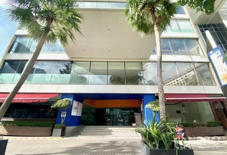 Retail Space for rent - Modern commercial building entrance in Bang Rak with glass facade, palm trees, and wide steps.