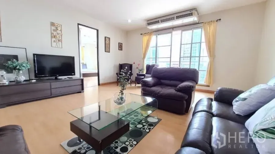 公寓 出租在Khlong Toei, Bangkok - 明亮客厅，真皮沙发、玻璃茶几、电视柜、木地板与大窗户俯瞰城市景观