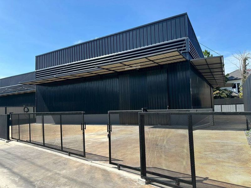 Warehouse for rent in Bueng Kum, Bangkok - Modern black metal-clad warehouse exterior with wide driveway, sliding mesh gate, and covered loading bay.