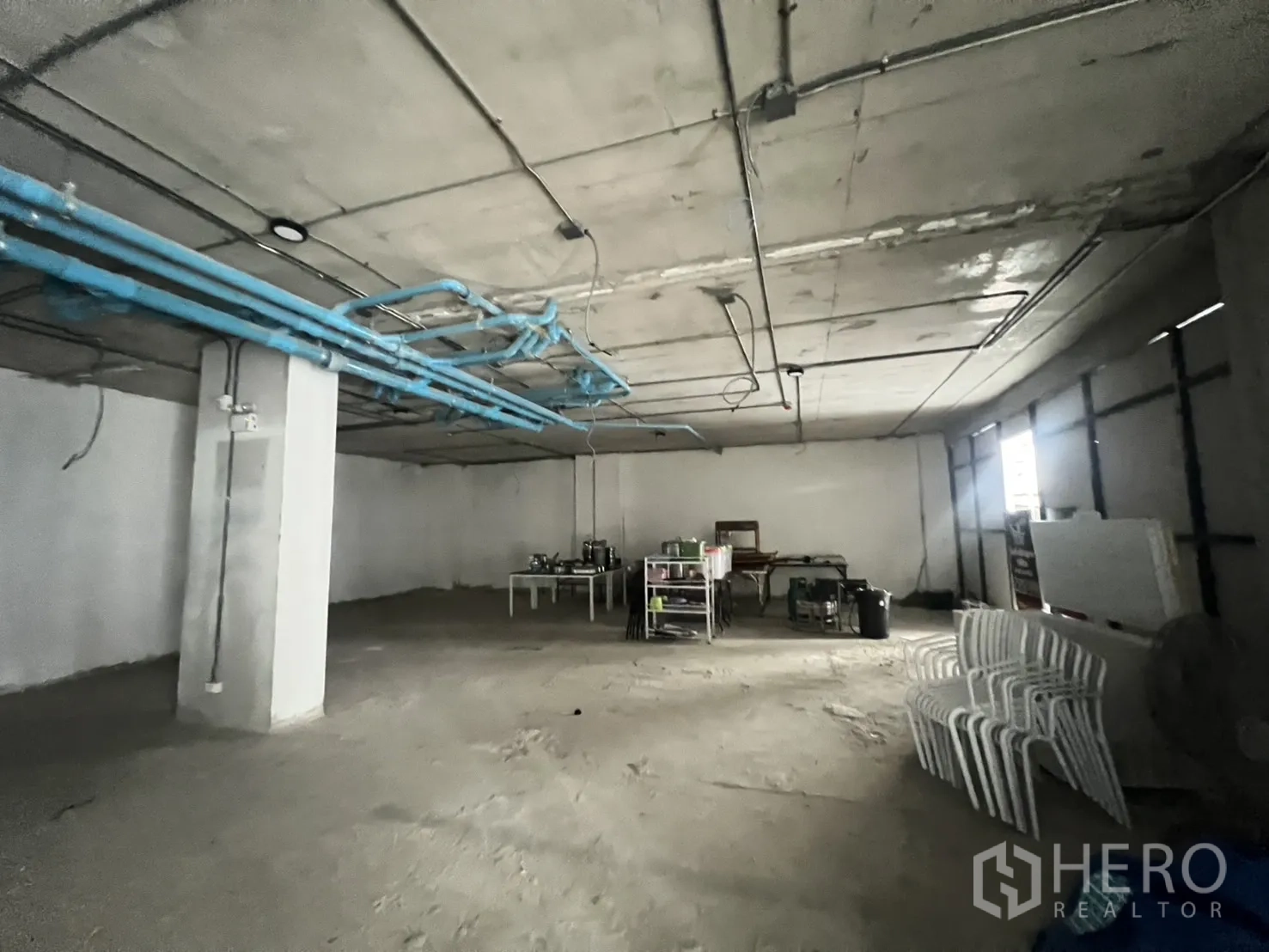 Retail Space for rent - Open-plan back-of-house area showing blue plumbing lines and concrete ceiling in an unfinished unit.
