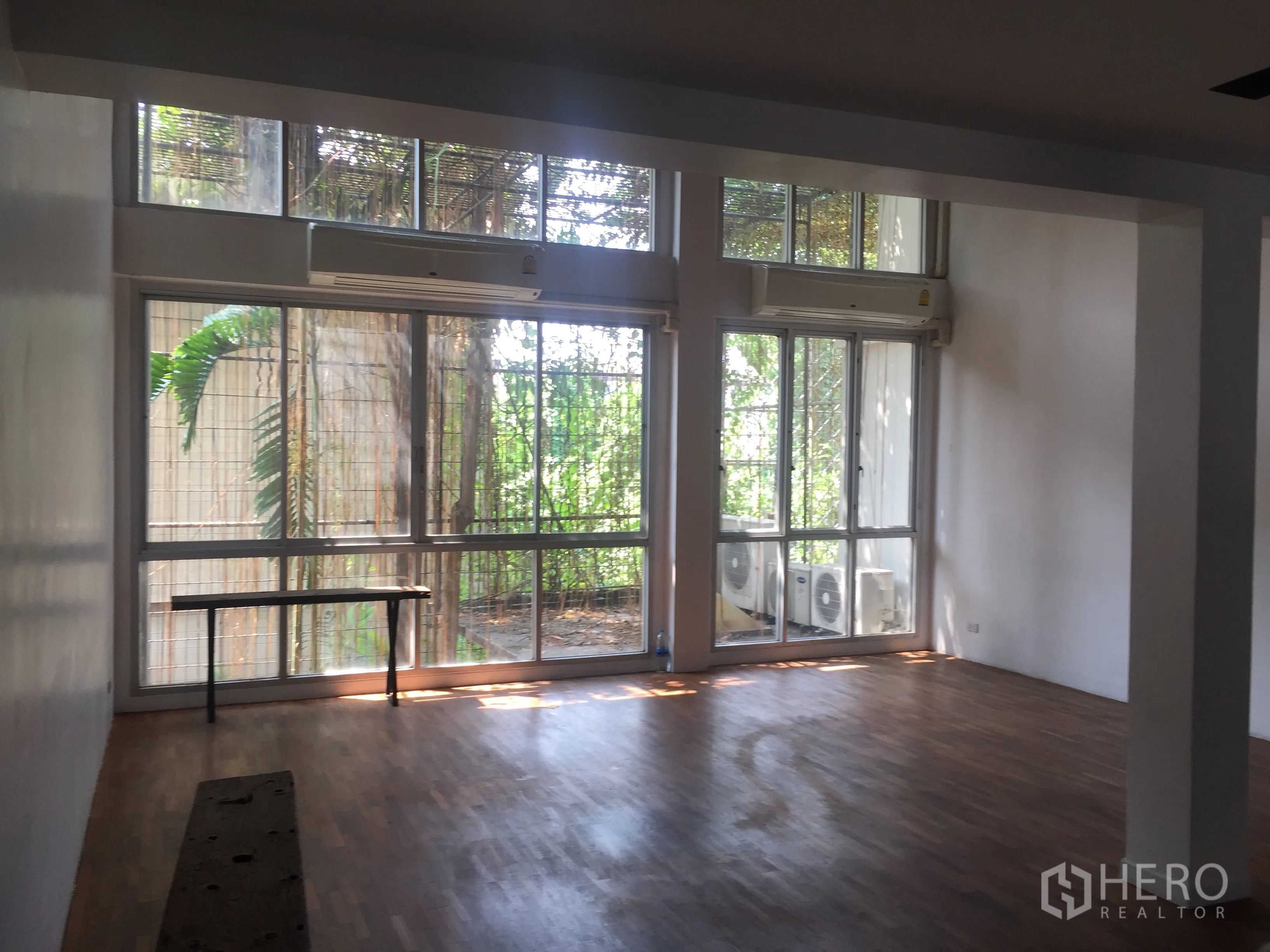 Townhouse for rent in Bang Rak, Bangkok - Spacious living room with floor-to-ceiling windows, hardwood flooring and green garden views in Silom.