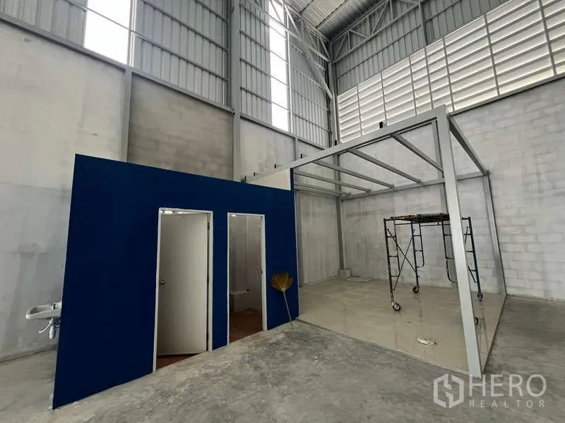 货栈 出租在Prawet, Bangkok - 仓库内部，高挑空间，蓝色隔间为办公室和卫生间，带钢制夹层框架。