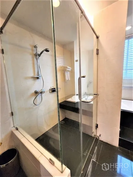 Condominium for rent in Bang Rak, Bangkok - Modern bathroom with glass-enclosed shower, handheld showerhead and vanity.
