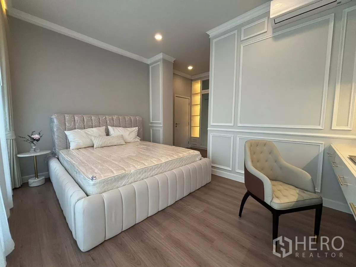 บ้าน ให้เช่าในBang Phli, Samut Prakan - ห้องนอนเตียงบุผ้านวม บัวผนัง และเก้าอี้แต่งตัว.