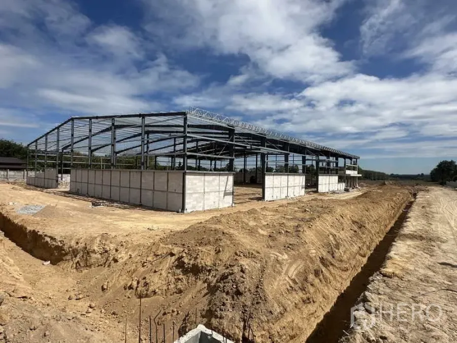 货栈 出租或出售在Nikhom Phatthana, Rayong - 更近距离展示仓库钢结构与混凝土基础墙，旁边为土路。