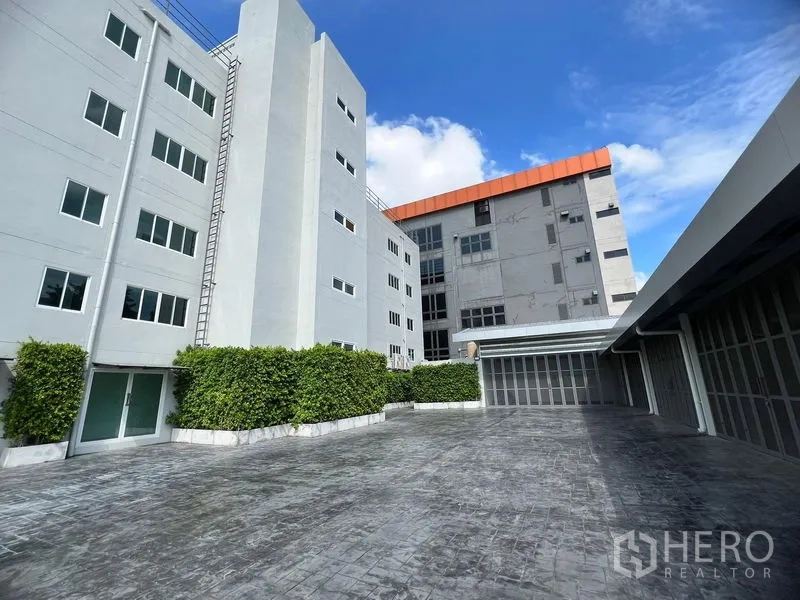 Retail Space for rent in Huai Khwang, Bangkok - Courtyard of modern low-rise buildings with grey facades, greenery and gated loading bays.