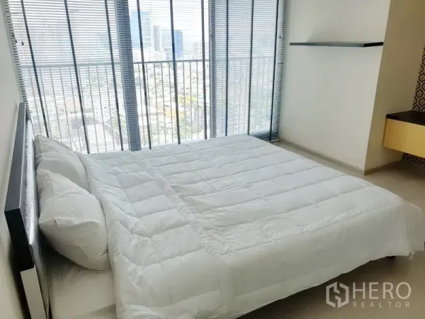 Condominium for rent in Khlong Toei, Bangkok - Sunlit bedroom with double bed, floor-to-ceiling windows with blinds, and skyline view.