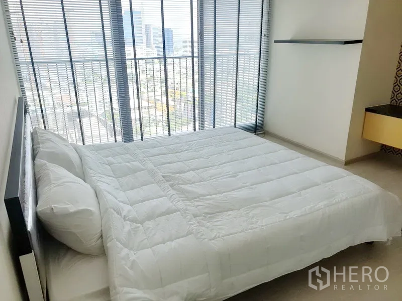 Condominium for rent in Khlong Toei, Bangkok - Sunlit bedroom with double bed, floor-to-ceiling windows with blinds, and skyline view.
