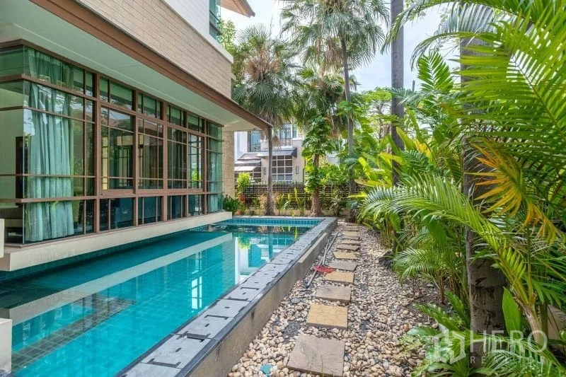 独立式住宅 出租在Watthana, Bangkok - 私家泳池沿屋侧延伸，热带花园与卵石小径相伴。