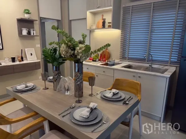 Townhouse for rent in Bang Phli, Samut Prakan - Dining area set for four beside a bright built-in kitchen with window blinds.