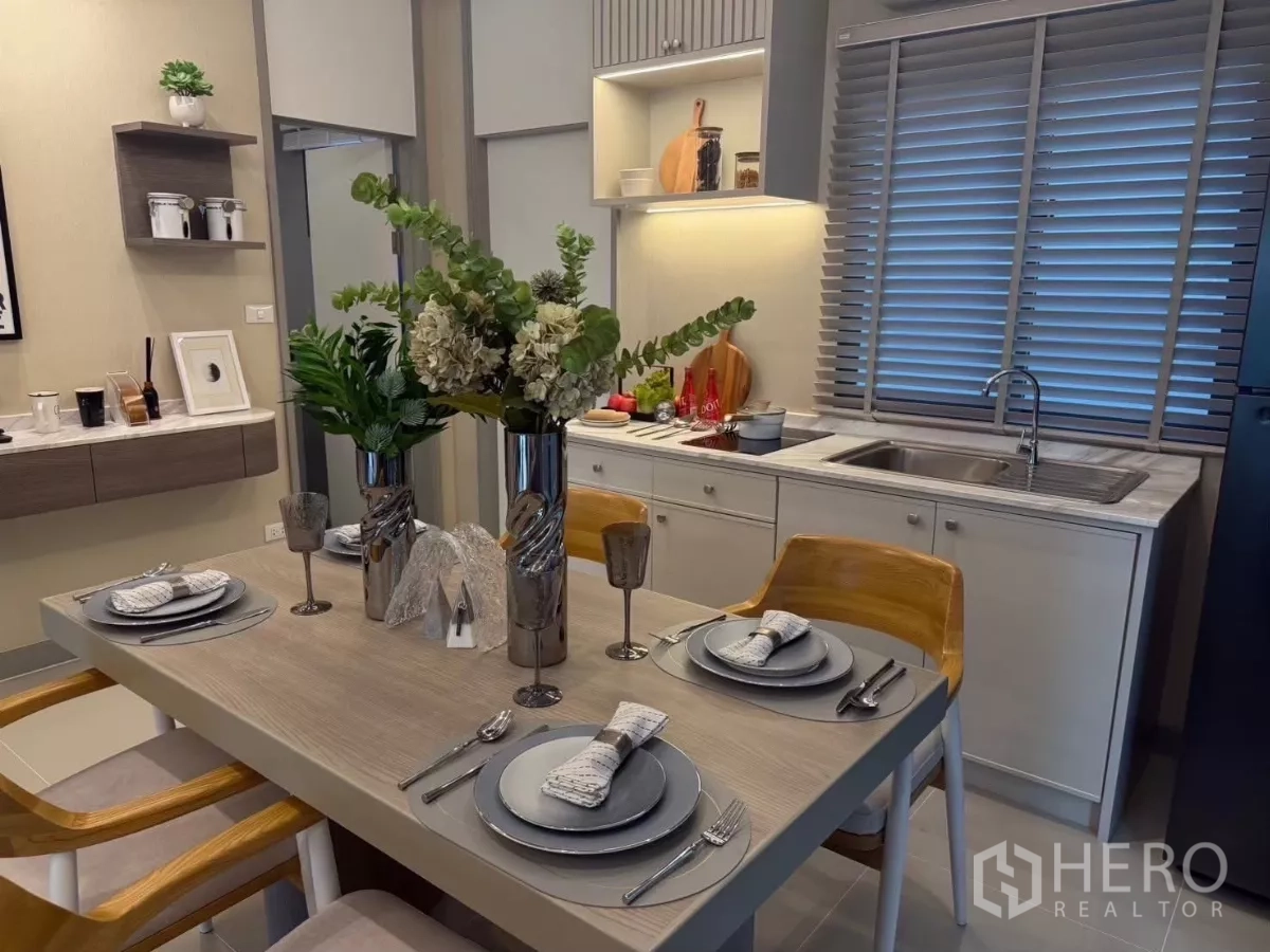 Townhouse for rent in Bang Phli, Samut Prakan - Dining area set for four beside a bright built-in kitchen with window blinds.
