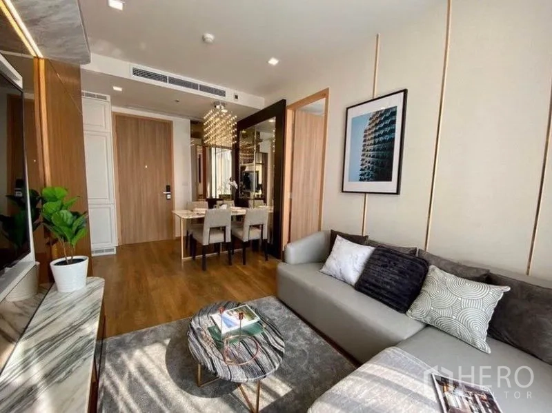 公寓 出租在Watthana, Bangkok - 瓦他那公寓明亮客厅，灰色沙发与大理石茶几，望向带吊灯的餐区。