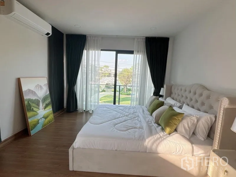 Detached House for rent or sale in Bang Phli, Samut Prakan - Spacious master bedroom with tufted headboard and sliding glass door opening to a balcony and green view.