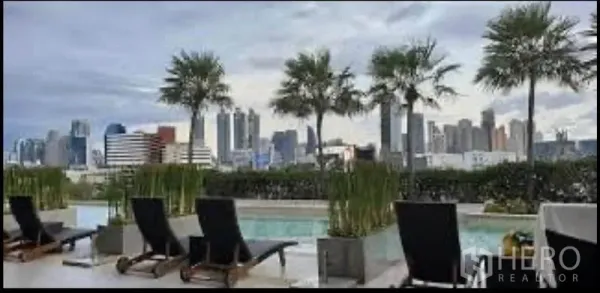 Condominium for rent in Sathon, Bangkok - Rooftop swimming pool with sun loungers and palm trees overlooking the Bangkok skyline.