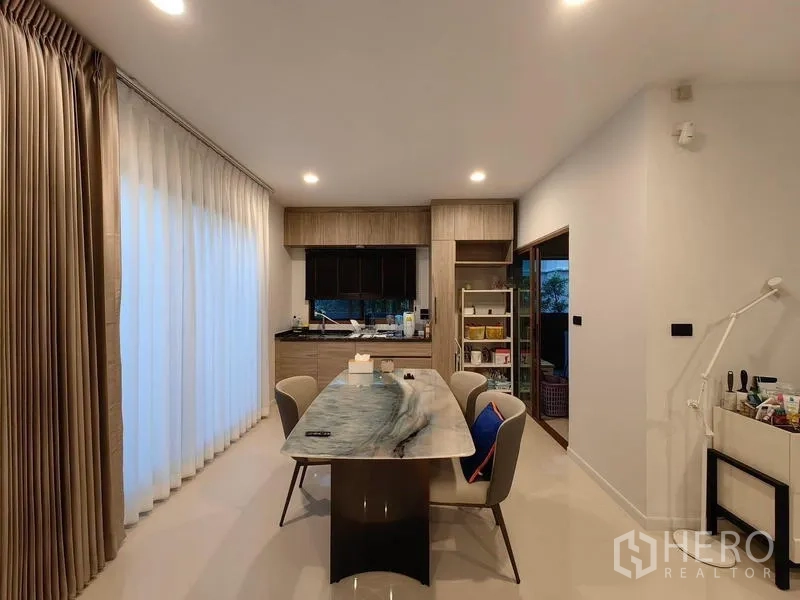 Detached House for rent in Bang Kapi, Bangkok - Dining area with large stone-top table next to pantry and full-height curtains