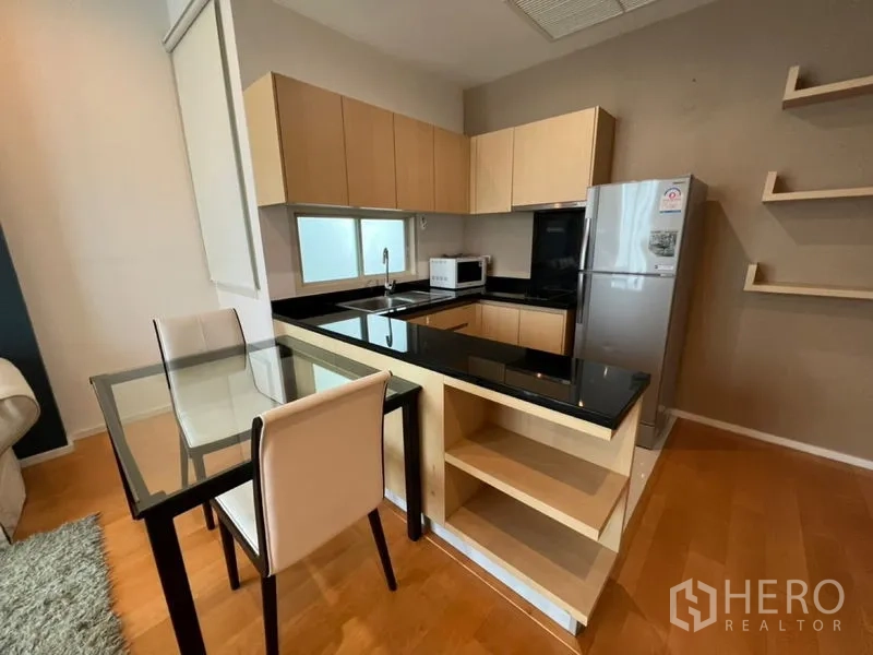 Condominium for rent in Chatuchak, Bangkok - Modern U-shaped kitchen with black granite counters, light wood cabinets and dining set