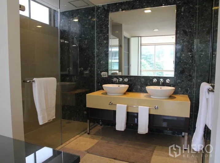 Condominium for rent in Khlong Toei, Bangkok - Modern bathroom with double vanity, vessel sinks, glass shower and large mirror.