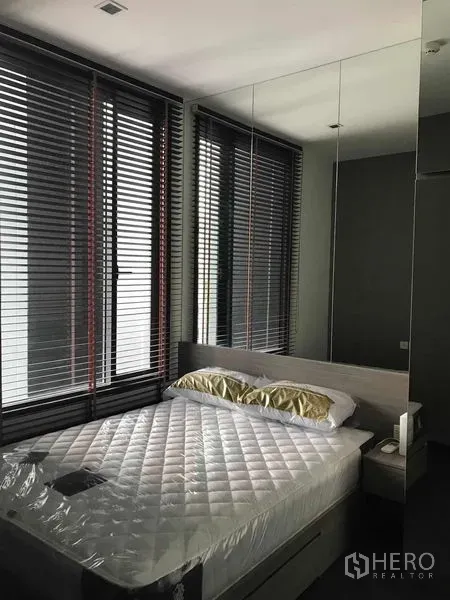 Condominium for rent in Watthana, Bangkok - Bright bedroom with a platform bed, mirrored wardrobe, and large windows with blinds.