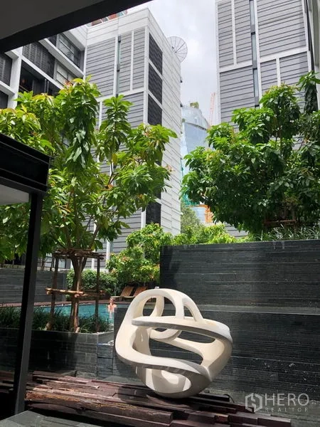公寓 出租在Watthana, Bangkok - 公寓庭院设有现代雕塑与绿化，可见泳池景观