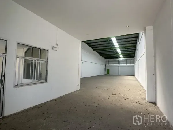 货栈 出租在Pathum Thani - 仓库内部宽敞，白色墙面，带玻璃隔断办公室与高挑金属屋顶天窗。