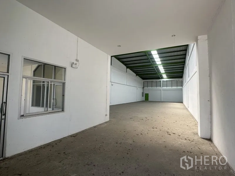 货栈 出租在Pathum Thani - 仓库内部宽敞，白色墙面，带玻璃隔断办公室与高挑金属屋顶天窗。
