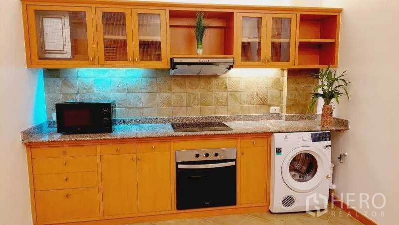 Apartment for rent - Kitchen countertop with built‑in oven, microwave shelf and washer beneath warm cabinetry.