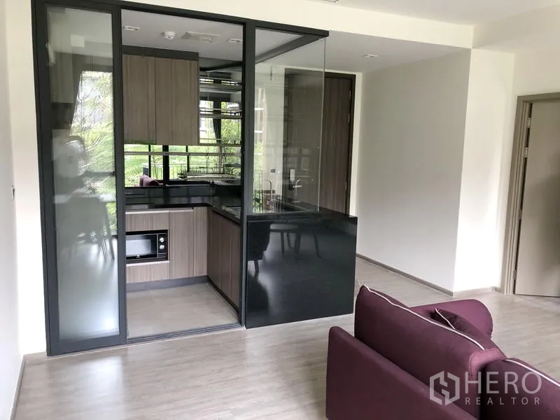 Condominium for rent in Watthana, Bangkok - Enclosed kitchen with glass partition, wood cabinetry, and black stone countertop with built-in microwave.
