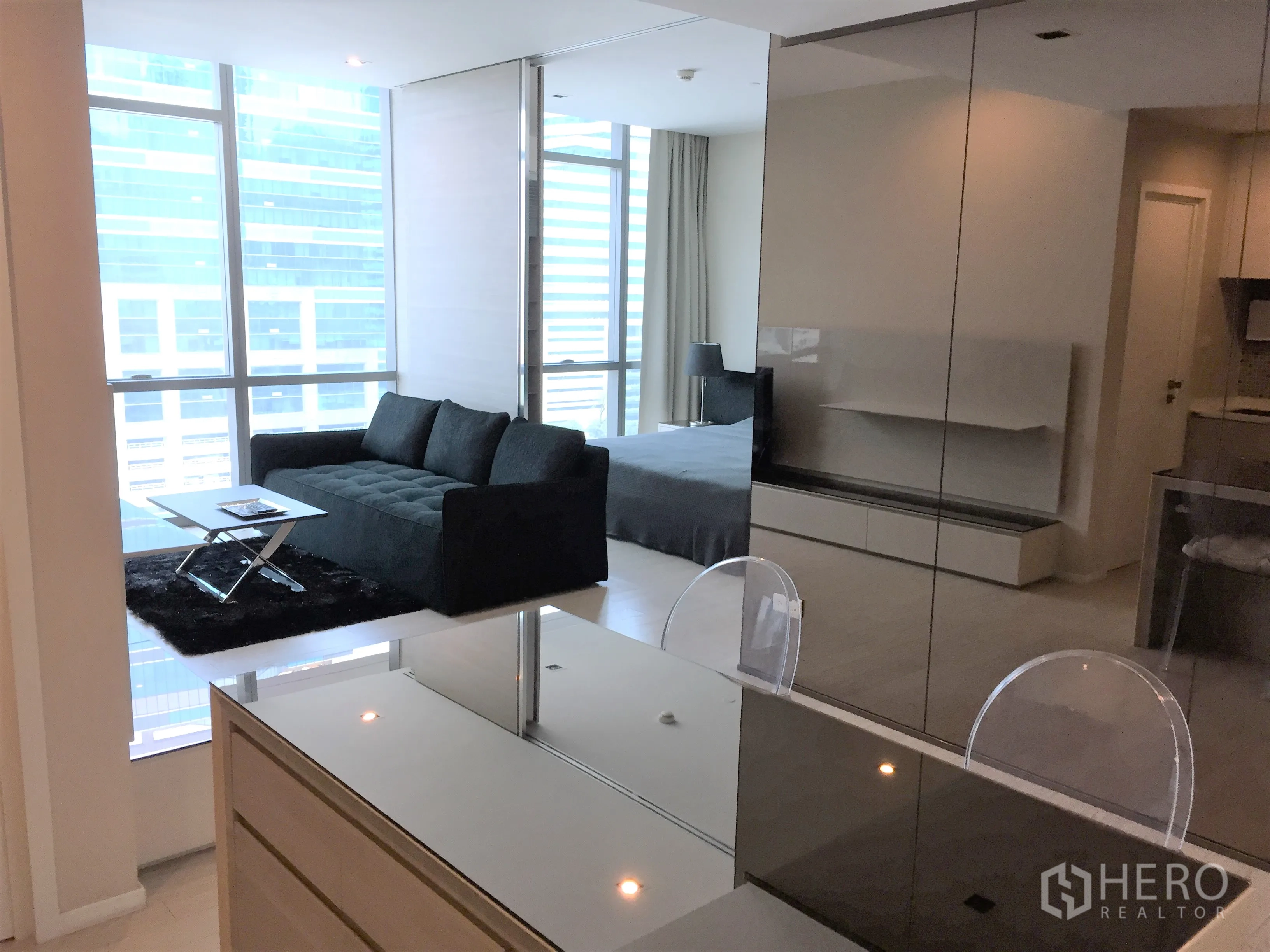 公寓 出租在Watthana, Bangkok - 客厅配黑色沙发与落地窗城市景，旁为亮面餐岛。