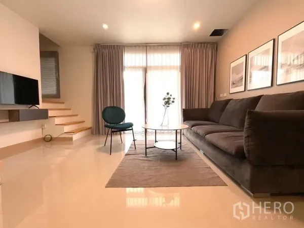 Townhouse for rent in Bang Phli, Samut Prakan - Spacious living room with large sofa, coffee table and staircase beside full-height windows.