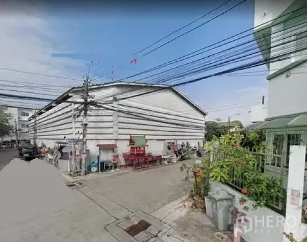 คลังสินค้า ให้เช่าในPrawet, Bangkok - มุมมองริมถนนของโกดังทรงจั่วสีขาวในซอยเงียบ เขตประเวศ กรุงเทพฯ มีสายไฟและบ้านพักอาศัยใกล้เคียง