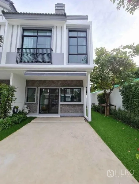Townhouse for rent in Bang Phli, Samut Prakan - Two-storey townhouse facade with driveway, big windows and landscaped garden.
