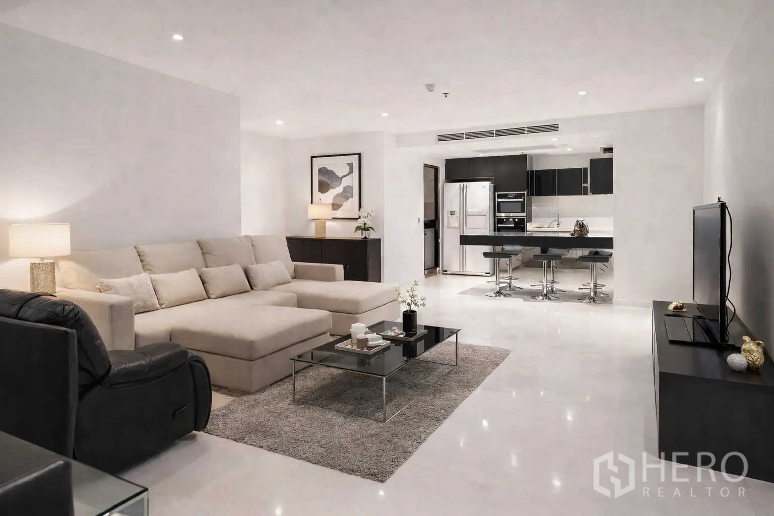 Condominium for rent in Watthana, Bangkok - Open-plan living room with beige sectional, recliner, and modern kitchen with breakfast bar.