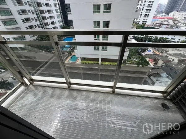 Condominium for rent in Khlong Toei, Bangkok - Private balcony with glass railing overlooking neighboring high-rise buildings and a pool below.