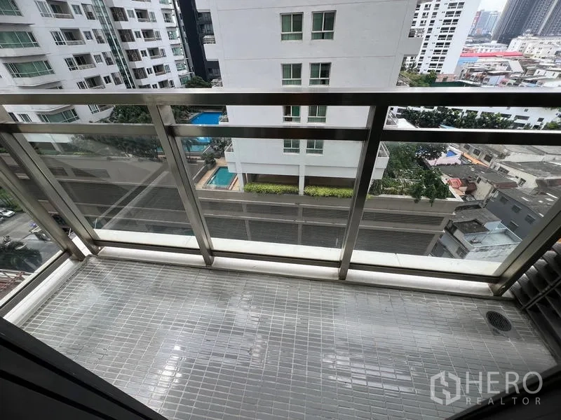 Condominium for rent in Khlong Toei, Bangkok - Private balcony with glass railing overlooking neighboring high-rise buildings and a pool below.