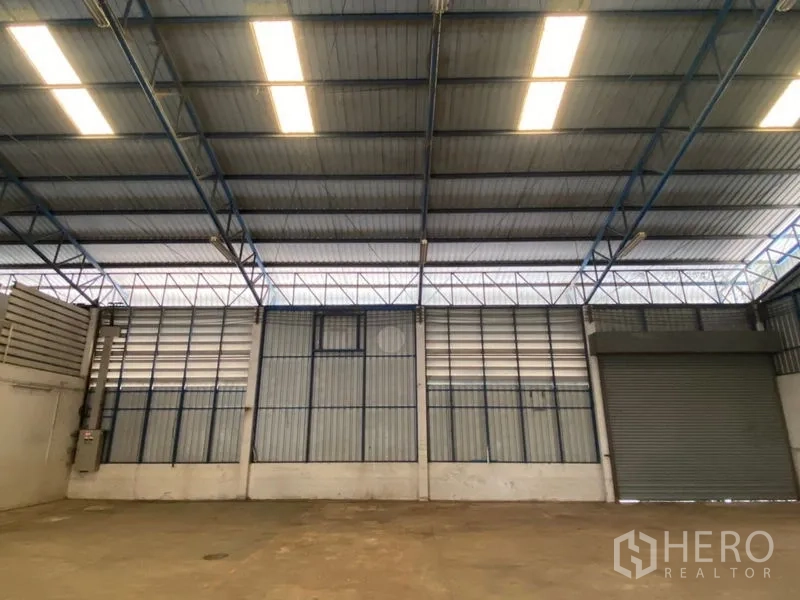 工厂 出租在Lat Lum Kaeo, Pathum Thani - 仓库墙面配照明与一扇卷闸门。