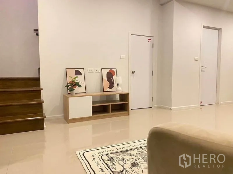 联排别墅 出租在Prawet, Bangkok - 客厅一角，电视柜、装饰画与木楼梯。