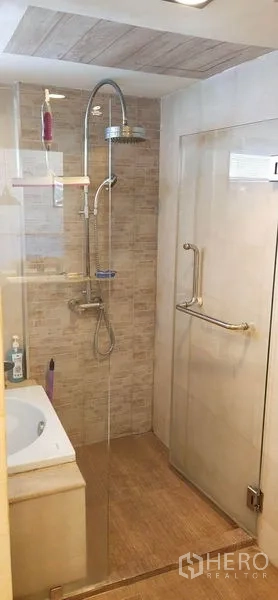 Condominium for sale in Watthana, Bangkok - Bathroom featuring glass shower enclosure with rain shower head and beige wall tiles.