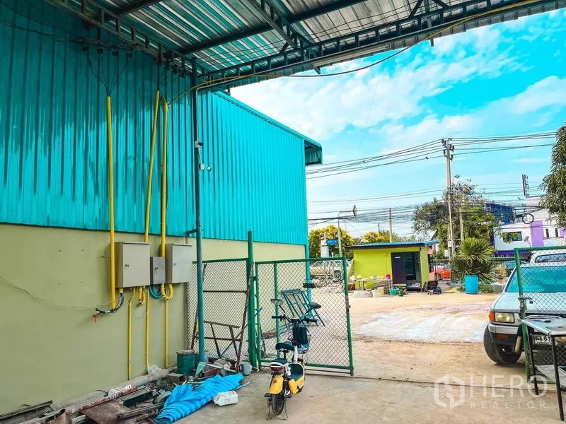货栈 出租在Sai Mai, Bangkok - 仓库侧院，带有雨棚装卸区、配电箱及围栏大门。