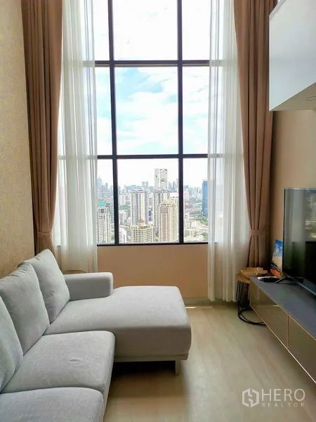 公寓 出租在Sathon, Bangkok - 客厅设落地窗与城市天际线景观，灰色转角沙发和电视柜。