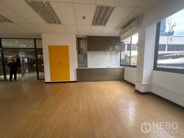 Office Space for rent in Bang Rak, Bangkok - Corner workspace with built-in cabinets, a yellow storage door, air-conditioning, and large windows.