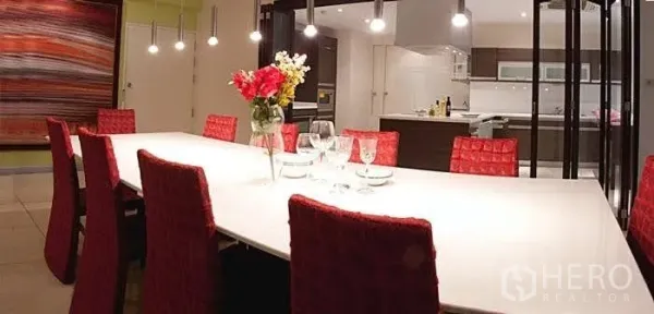 Condominium for rent in Yan Nawa, Bangkok - Contemporary dining room with a long white table, red chairs and pendant lighting beside the open‑plan kitchen.