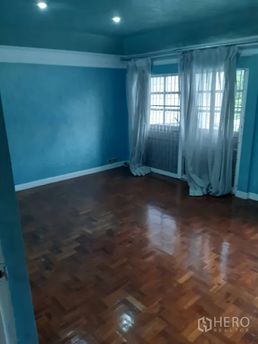 联排别墅 出租在Khlong Toei, Bangkok - 蓝色墙面与拼花木地板的房间，大窗与薄纱窗帘。