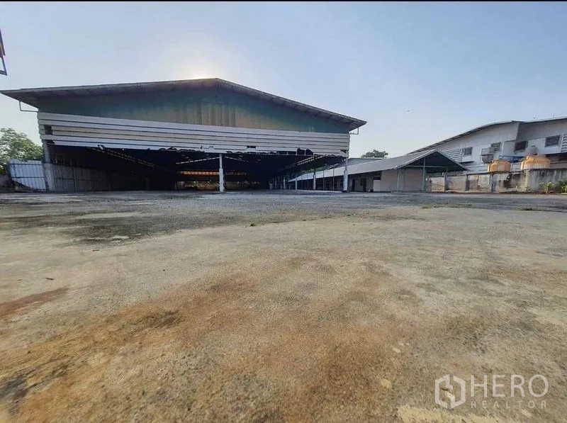 Warehouse for rent or sale in Mueang Pathum Thani, Pathum Thani - Front view of a large metal-clad warehouse with an expansive loading and turning yard.