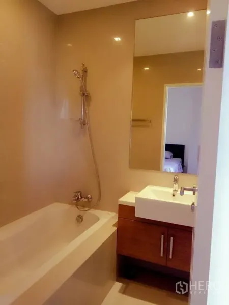 Condominium for rent in Bangkok - Modern bathroom with bathtub, handheld shower, vanity and mirror in a Bangkok condo.