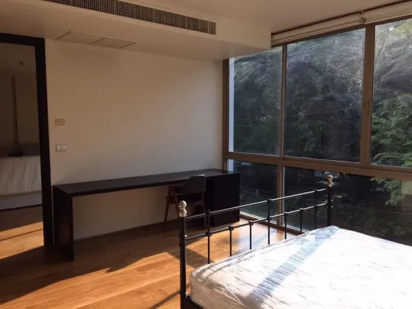 Condominium for rent in Khlong Toei, Bangkok - Bedroom workspace with long built-in desk, metal bed, and expansive windows with green views.