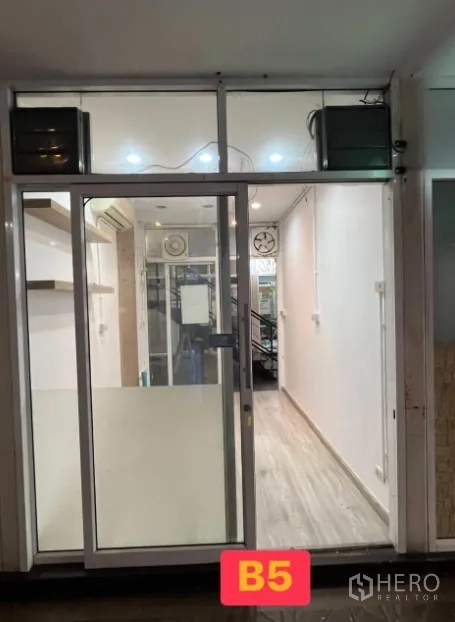零售空间 for rent in Watthana, Bangkok - 小型商铺，玻璃推拉门，明亮顶灯与浅色木纹地板，标注 B5。