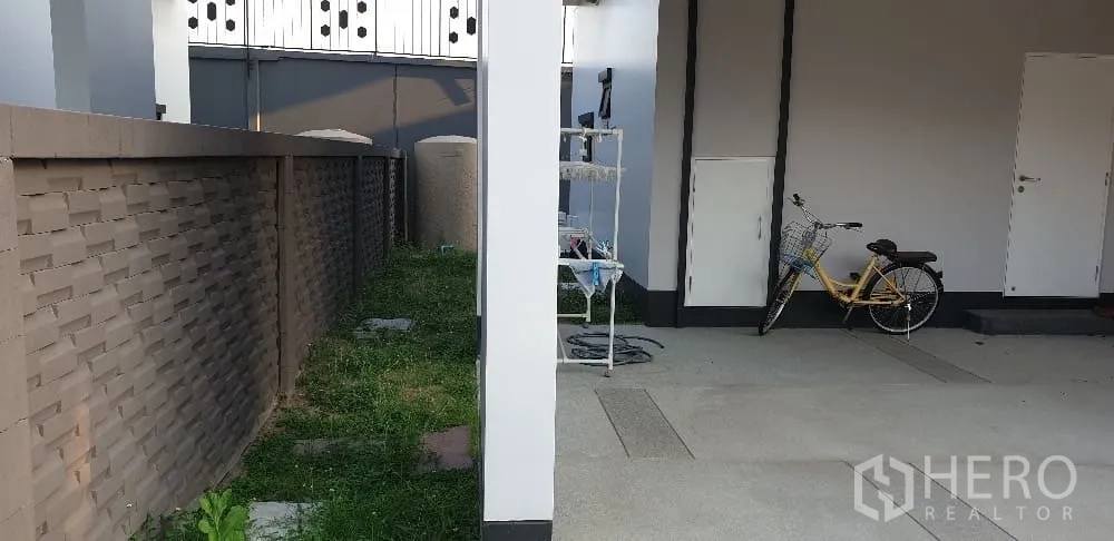 Detached House for rent or sale in Lam Luk Ka, Pathum Thani - Side yard and covered carport with storage doors and bicycle.